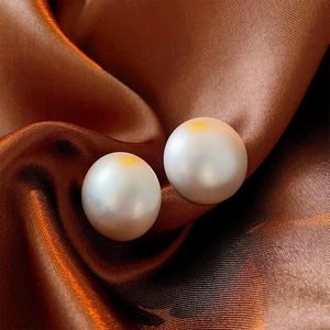 Macro shot of elegant white round pearl earrings on luxurious brown silk fabric