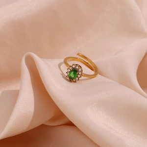 Detail of adjustable gold ring with oval green gemstone and zircon halo on pink silk
