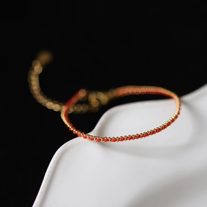 Macro shot of handmade red string bracelet with gold beads on a ceramic plate