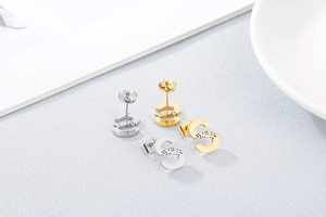 Detail of silver and gold S-shaped earrings with SMILE cutout on a textured surface