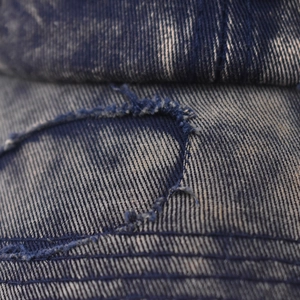 Close-up of distressed denim baseball cap showing torn details and twill texture