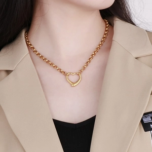 Dettaglio di una collana con ciondolo a cuore dorato e catena a maglie su una modella