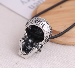 Macro view of vintage silver skull pendant with intricate floral engravings and black cord