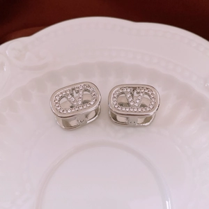 Detailed view of silver V-logo earrings with micro-pave zircons on a ceramic plate