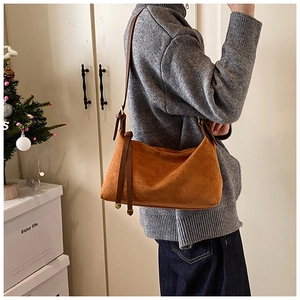 Detailed side view of a brown suede hobo shoulder bag worn by a model in a cozy setting