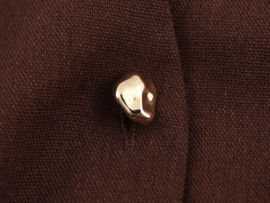 Macro shot of an irregular gold pebble button on dark brown knitted linen dress fabric