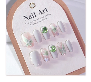 Detail of 3D floral cat-eye press-on nails with butterfly motifs and green rhinestones