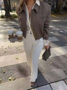 Dettaglio di una giacca in tweed marrone sfiancata abbinata a pantaloni bianchi chic