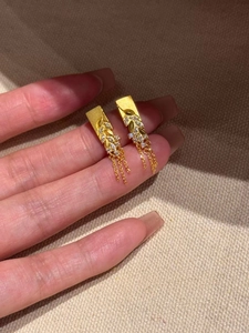 Detailed view of gold plated leaf earrings with zircon tassels held in hand