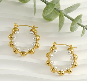 Détail des boucles d'oreilles ondulées plaquées or 18k avec perles sur fond texturé
