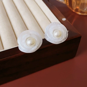 Detailed view of white rose petal earrings with pearls on a vintage wooden jewelry stand