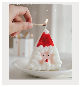 Gros plan d'une main allumant une bougie parfumée en forme de Père Noël sur un plateau