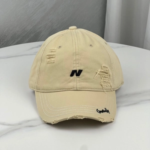 Detailed view of beige distressed cotton baseball cap with embroidered letter N and frayed brim