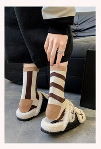 Detail of striped knitted crew socks in brown and beige tones worn with plush slippers