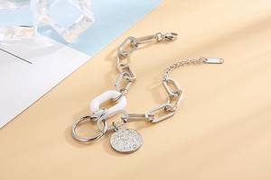 Détail d'un bracelet chaîne argentée avec un pendentif pièce ronde à texture martelée