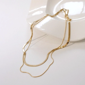Zweilagige goldene Schlangenknochenkette auf einem weißen minimalistischen Keramikteller