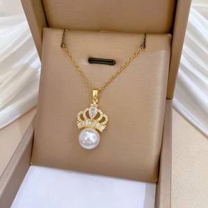 Detailed close-up of a golden crown pendant necklace with a large pearl in a jewelry box