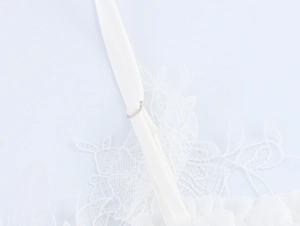 Detailed close-up of white lace fabric with handmade floral embroidery and silver buckle