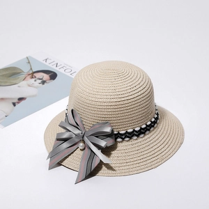 Detail of a beige straw sun hat featuring a stylish striped ribbon bow and pearl accent.