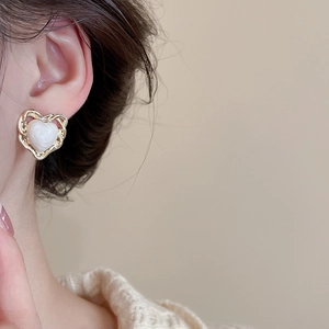 Detailed view of heart-shaped gold earring with white opal stone on female ear