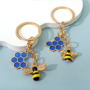 Close-up of golden bee keychain with blue honeycomb pendant on white display stand