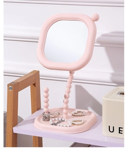 Detail shot of pink cream-style vanity mirror with rotatable beaded stand and jewelry tray.