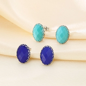 Minimalist oval glass stud earrings in blue with silver claw settings on beige silk