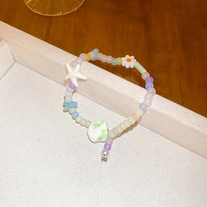Detail of colorful matte ceramic beaded bracelet with floral and star charms on a white tray