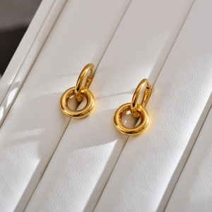 Detailed close-up of detachable double-ring gold hoop earrings on a white leather texture