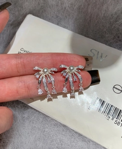 Detail of silver bow pearl earrings with crystal water drop pendant held in hand