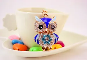 Close-up of owl keychain with blue enamel and sparkling crystals on a cream cup