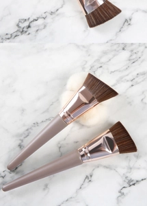 Angled foundation brush with soft brown bristles and rose gold ferrule on marble