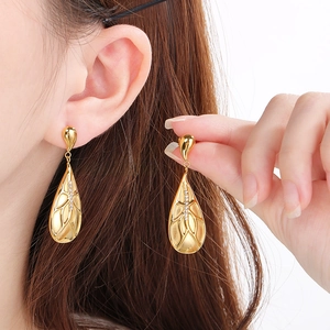 Golden teardrop earrings with textured surface and white crystal inlay on a model