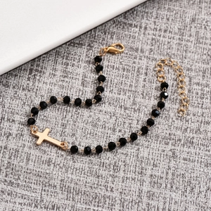 Macro detail of minimalist black beaded bracelet with gold cross and lobster clasp