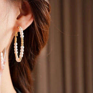 Detail of large hoop earrings with alternating pearls and golden beads on model