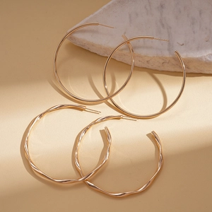 Minimalist geometric gold hoop earrings with twisted and smooth finishes on a marble base