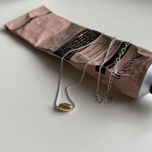 Minimalist 925 sterling silver beaded necklace with a golden oval pendant on Aesop tube