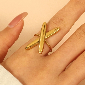 Macro shot of gold-plated X-shaped ring on model's finger with smooth metallic finish