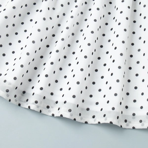 Macro shot of white chiffon fabric with black polka dots showing hem and soft drape texture