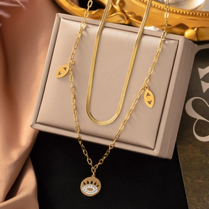 Detail of layered gold titanium necklace with evil eye pendant on elegant silk background