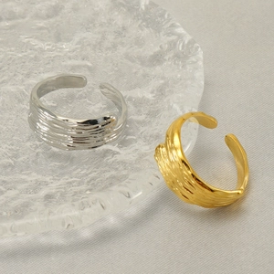 Adjustable stainless steel rings in gold and silver with lava texture on glass plate