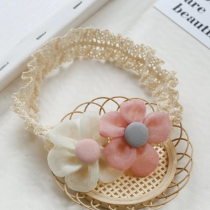 Lace baby headband with pink and white fabric flowers on a woven basket