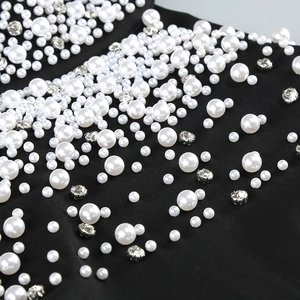 Detailed view of artificial pearls and sparkling rhinestones on black evening dress fabric