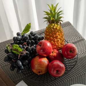 Artificial fruit set with red apples and black grapes in a black wire metal basket