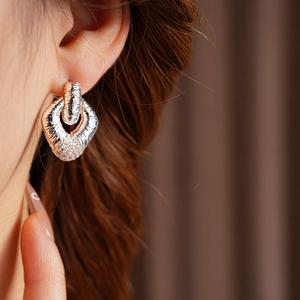 Close-up of a textured silver geometric earring with sparkling diamond accents on a model