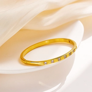 Elegant gold titanium steel bangle with inlaid zircons on a white display tray