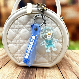 Blue astronaut quicksand keychain with Dream On strap displayed on a white quilted handbag