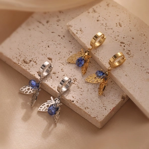 Macro view of gold and silver bee earrings with blue gemstones on elegant textured fabric