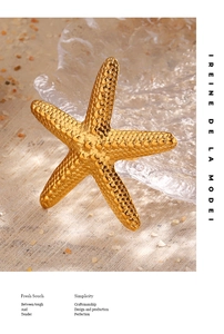 Close-up of golden starfish ring with grainy texture on sand and glass background
