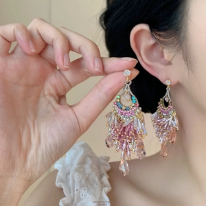 Vue macro de boucles d'oreilles bohèmes avec perles roses et pompons en émail coloré